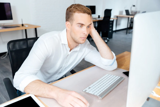 un jeune homme ennuyé travaille devant son ordinateur